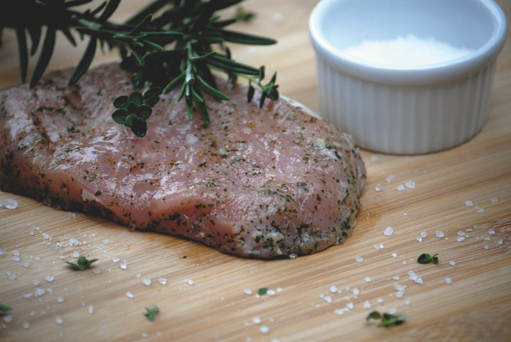 Foto eines rohen marinierten Kalbsteak der Gassner GmbH, präsentiert auf einem Holzbrett, dekoriert mit groben Salz und Rosmarin