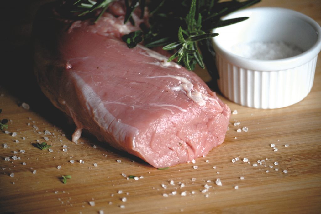 Foto eines rohen Kalbsbraten, präsentiert auf einem Holzbrett, dekoriert mit groben Salz und Rosmarin