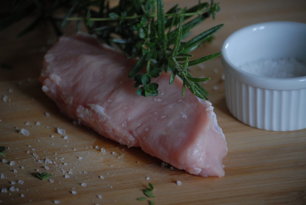 Foto eines rohen Kalbsfilet der Gassner GmbH, präsentiert auf einem Holzbrett, dekoriert mit groben Salz und Rosmarin